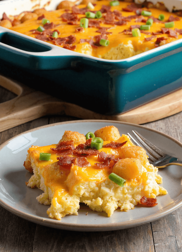 Serving of bacon, egg, and tater tot casserole topped with cheddar cheese, bacon, and chopped green onions on a gray plate.