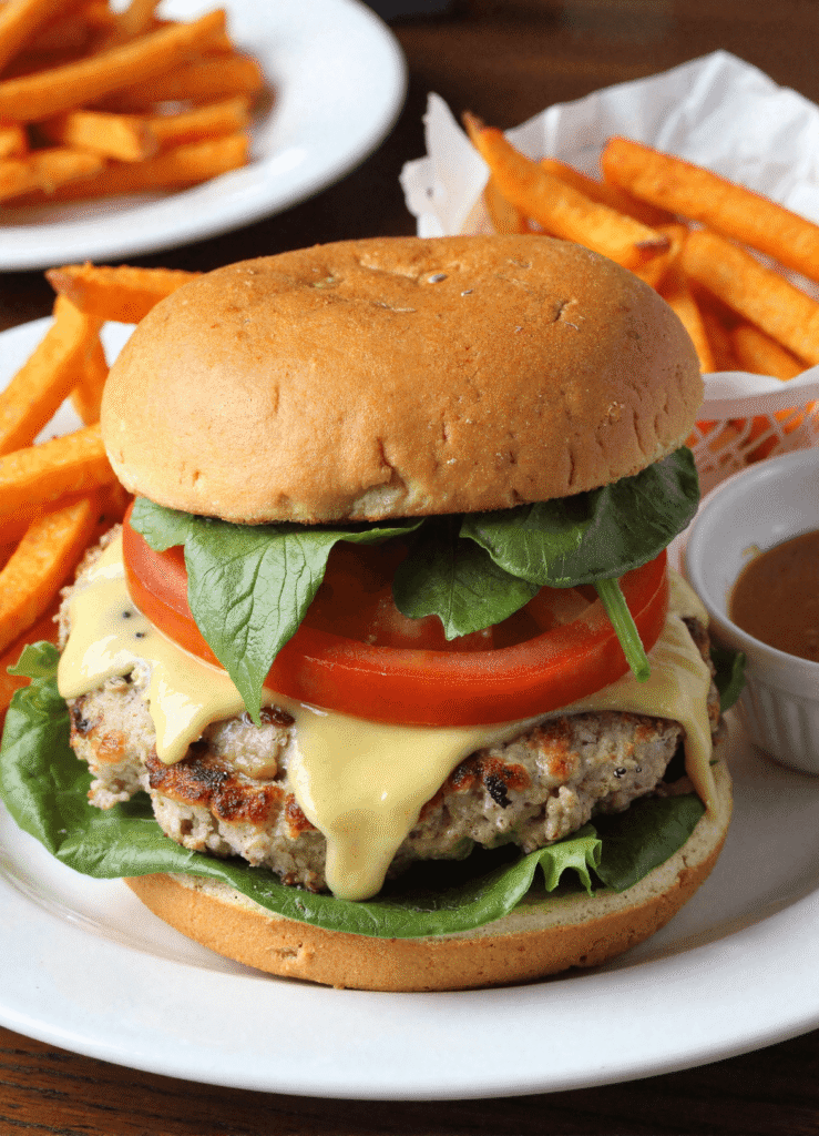 White cheddar spinach chicken burger with tomato and lettuce served with sweet potato fries on a white plate