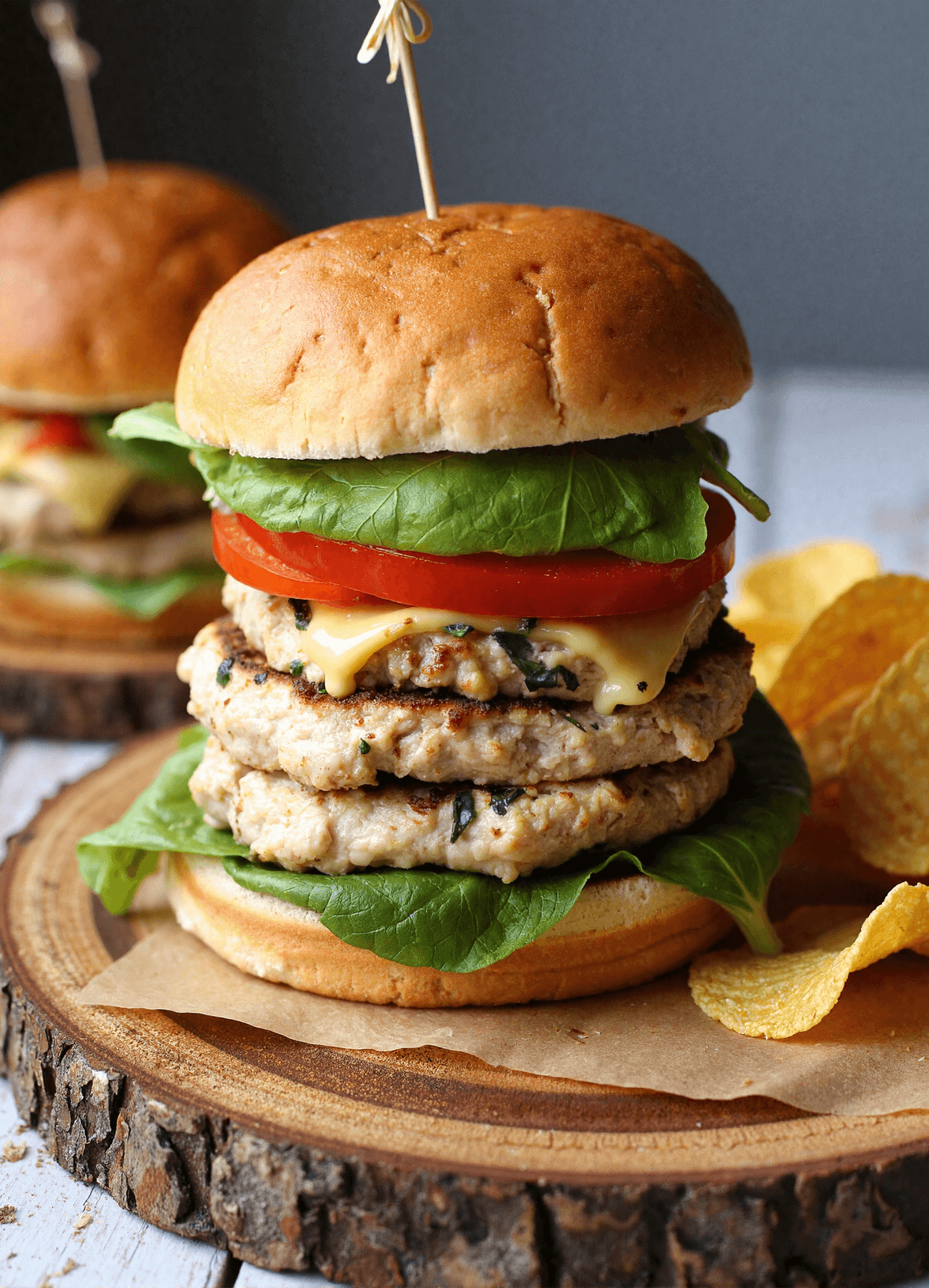 Stacked white cheddar spinach chicken burgers with lettuce and tomato on toasted buns served with potato chips
