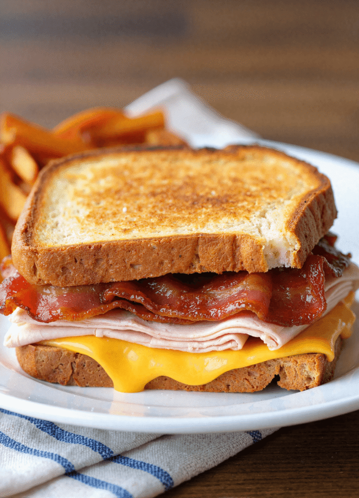 Cheddar and bacon turkey melt sandwich with golden sourdough, melted cheddar, crispy bacon, and sliced turkey served with fries