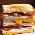 Stacked cheddar and bacon turkey melt on sourdough bread with gooey cheddar, crispy bacon, and sliced turkey breast