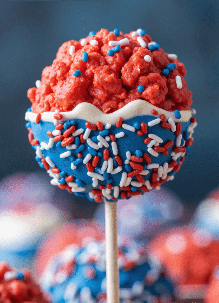 Close-up of a red Firecracker Rice Krispies Pop dipped in blue and white candy melt and coated with patriotic sprinkles on a stick
