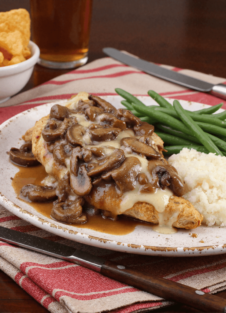 Plate of copycat Texas Roadhouse smothered chicken topped with melted cheese and mushrooms, served with mashed cauliflower and green beans.