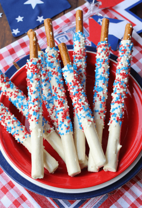 Red, white, and blue candy-dipped pretzel rods on a red plate for a festive Fourth of July dessert