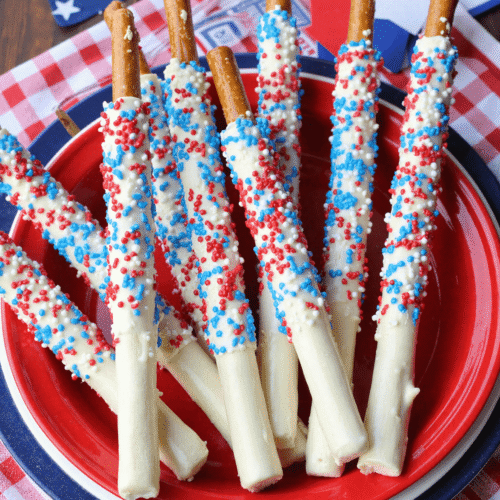 Red, white, and blue candy-dipped pretzel rods on a red plate for a festive Fourth of July dessert