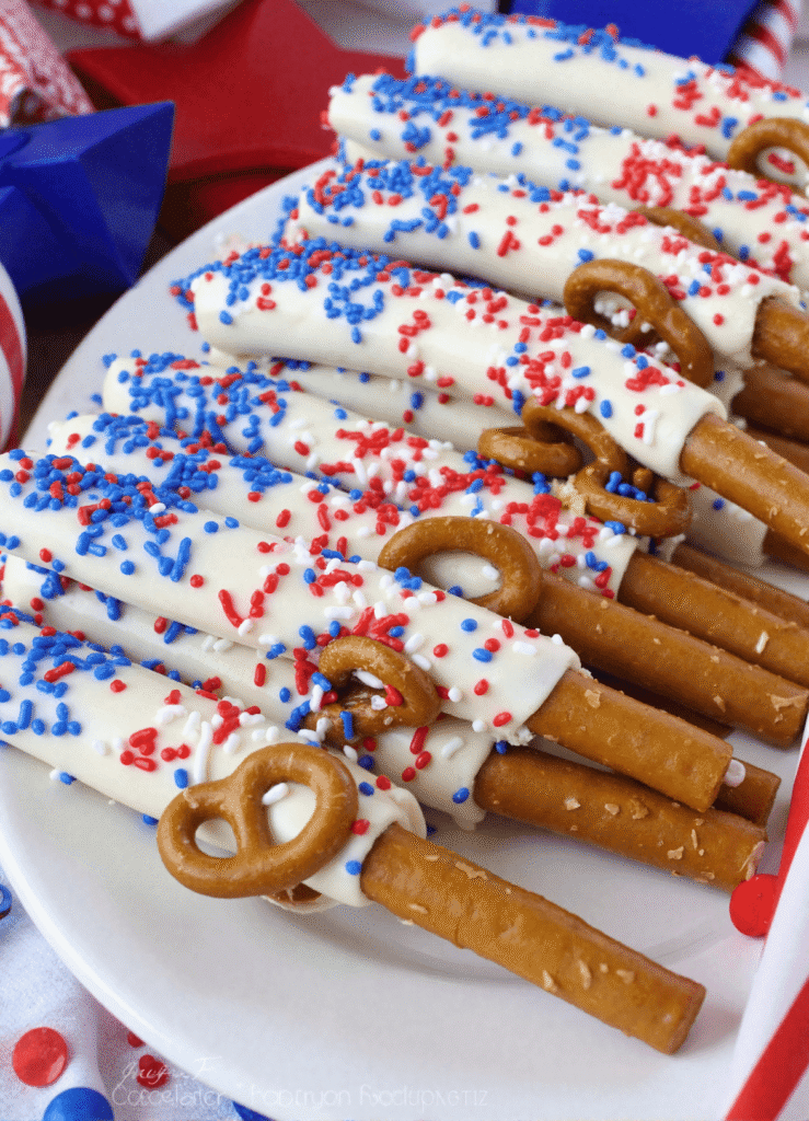Fourth of July pretzel rods coated in white candy and topped with colorful red, white, and blue sprinkles