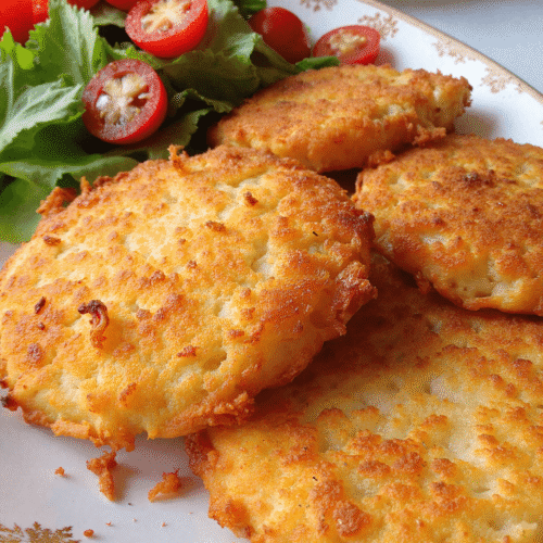 Healthy crispy hashbrowns plated with fresh salad greens and cherry tomatoes on a vintage dish.
