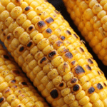 Charred lemon pepper corn on the cob glistening with melted butter and cracked black pepper.