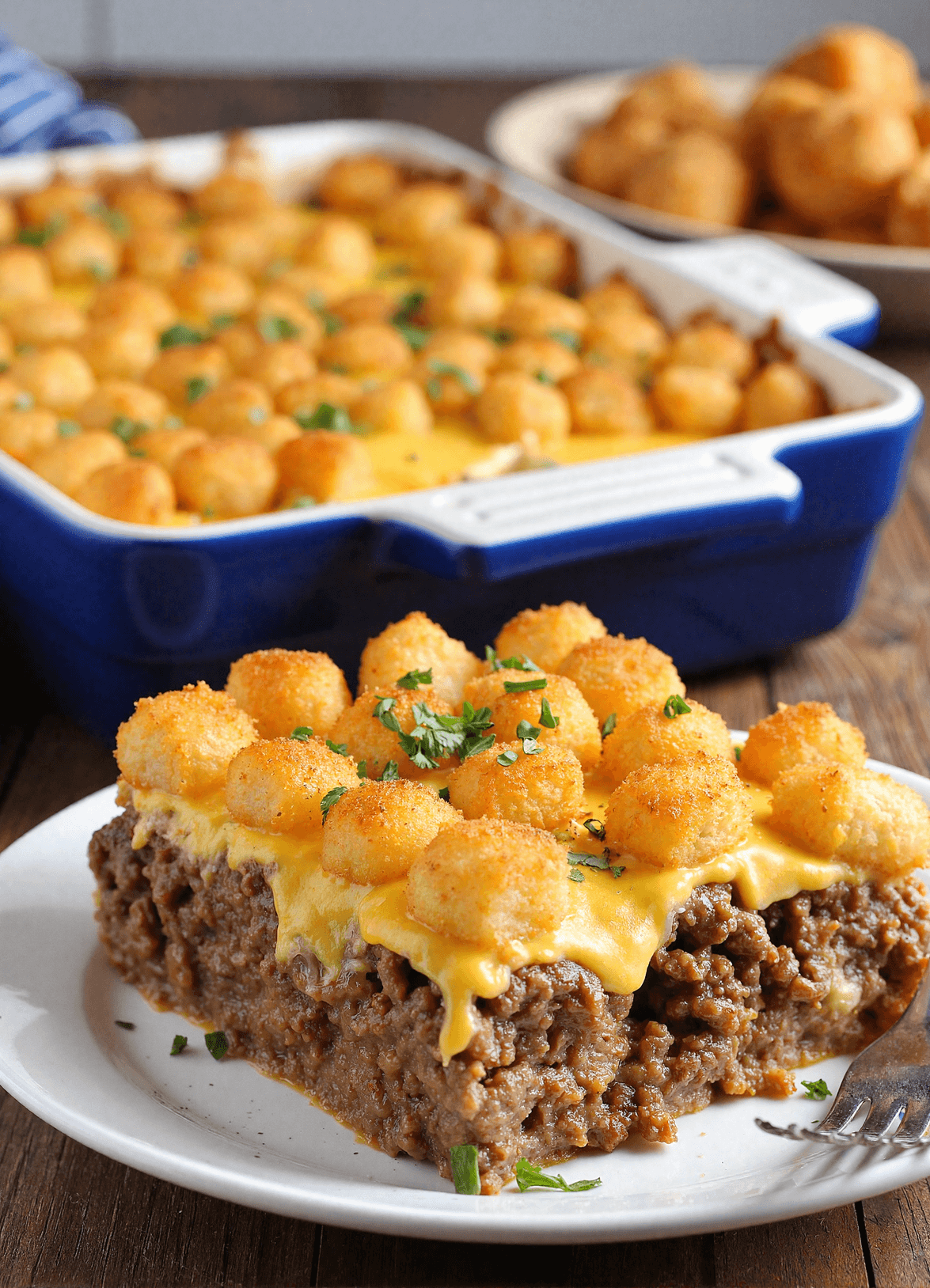 Loaded cheeseburger tater tot casserole featuring ground beef, mixed vegetables, crispy tater tots, melted cheese, and fresh parsley served on a ceramic plate.