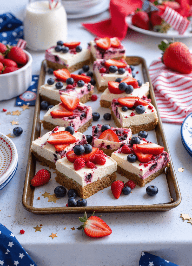 Tray of no-bake patriotic cheesecake bars topped with strawberries and blueberries for Independence Day