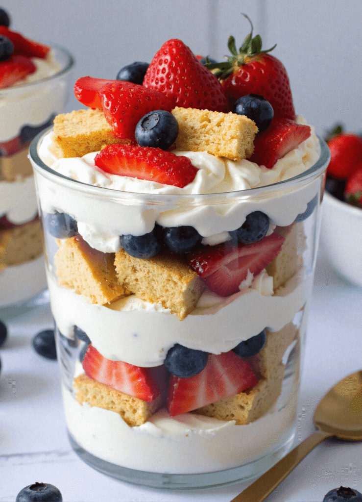 Close-up of a single patriotic berry shortcake trifle with layers of whipped cream, blueberries, strawberries, and golden pound cake in a glass jar.