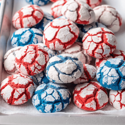 Red and blue patriotic crinkle cookies with powdered sugar on a tray for a Fourth of July dessert.