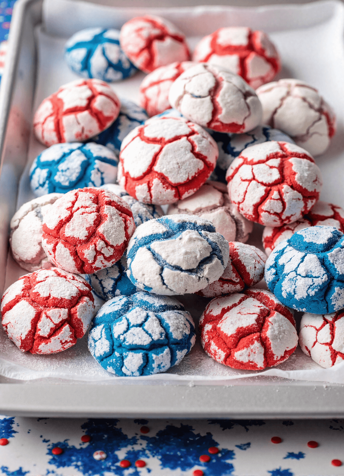 Red and blue patriotic crinkle cookies with powdered sugar on a tray for a Fourth of July dessert.