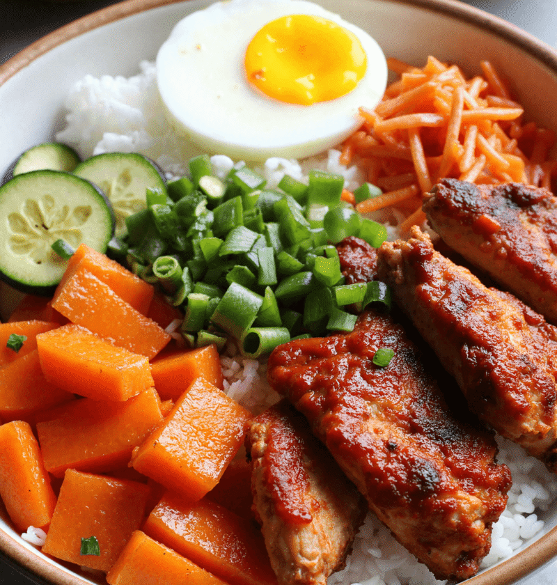 Spicy Korean BBQ chicken rice bowl with sesame seeds, hard-boiled egg, julienned carrots, zucchini, and jasmine rice.
