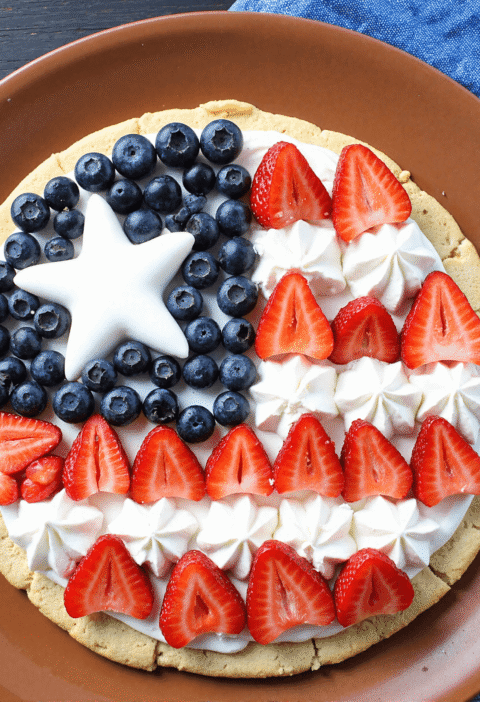 Patriotic stars and stripes fruit pizza topped with blueberries, strawberries, and piped whipped cream stars on a sugar cookie crust.