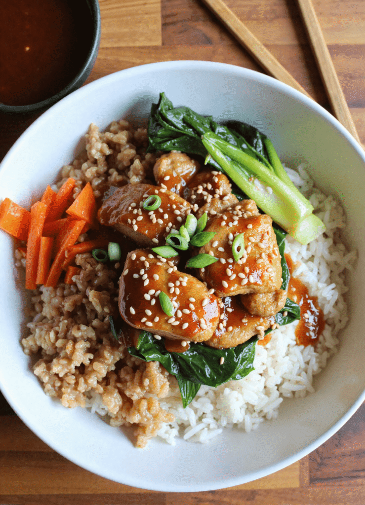Sticky ginger tofu over white rice and brown rice, served with bok choy, sesame seeds, and julienned carrots.