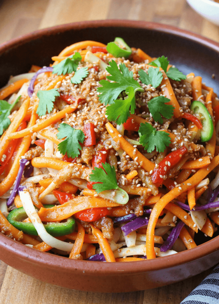 Sweet and spicy Asian slaw featuring red cabbage, carrots, bell peppers, and sliced jalapeños tossed in sesame vinaigrette