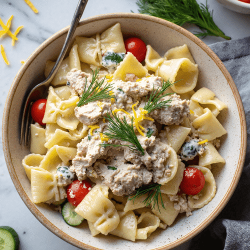 Healthy tuna pasta salad with lemon and dill, cherry tomatoes, cucumber, and creamy dressing in a ceramic bowl