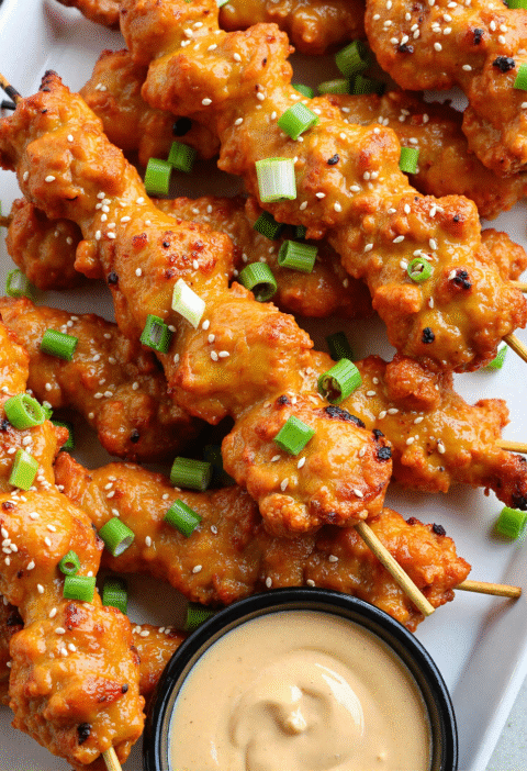 Close-up of grilled Bang Bang Chicken Skewers with caramelized edges, coated in sweet and spicy Bang Bang sauce, served with lime wedges and fresh cilantro.