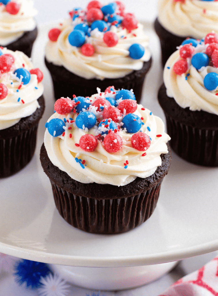 Chocolate firecracker cupcakes topped with white frosting and red, white, and blue popping candy for a festive 4th of July dessert.