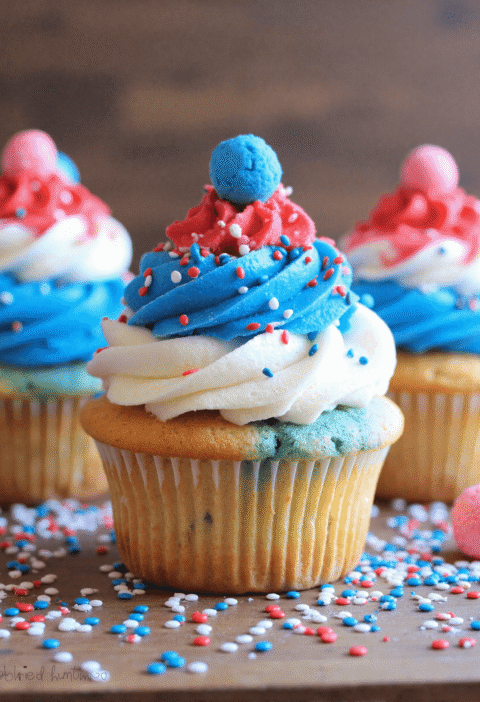 Red, white, and blue firecracker cupcake topped with patriotic frosting swirl and candy, decorated with sprinkles.
