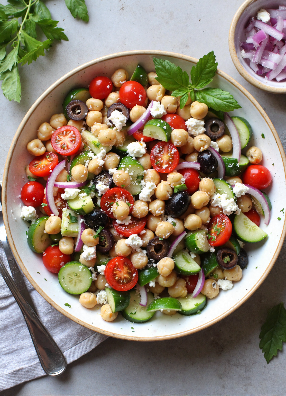 No-cook Mediterranean chickpea salad with cucumber, cherry tomatoes, olives, feta cheese, and fresh parsley on a white plate.