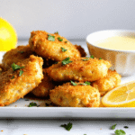 Golden lemon chicken bites served on a white plate with lemon dipping sauce and parsley garnish.