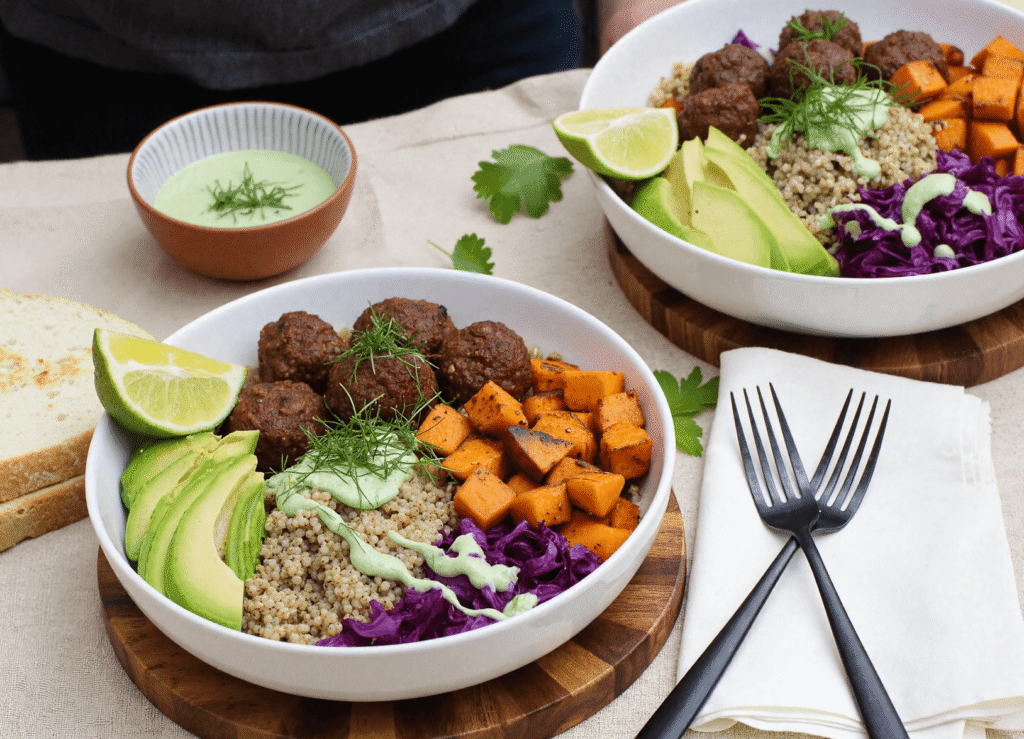 Barbecue meatball bowl with roasted sweet potatoes, quinoa, avocado slices, and green goddess dressing in a white bowl on a wooden board.