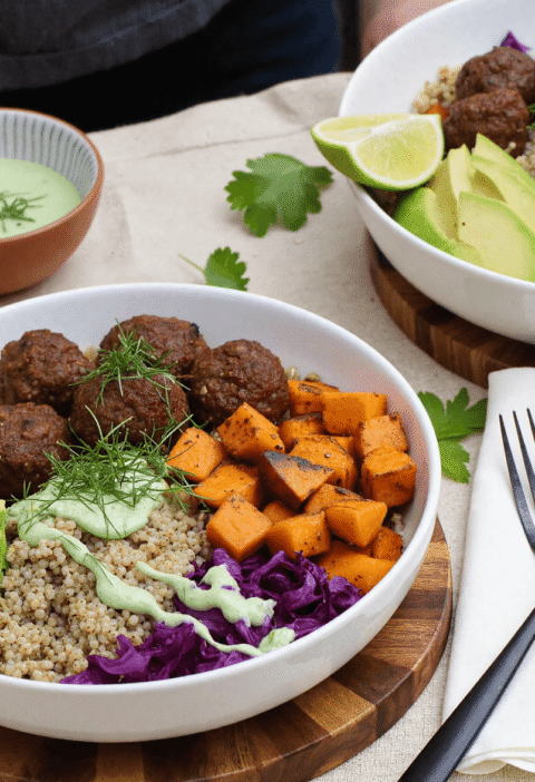 High-protein dinner bowl featuring barbecue meatballs, sweet potatoes, quinoa, fresh avocado, and herbs served in ceramic bowls.