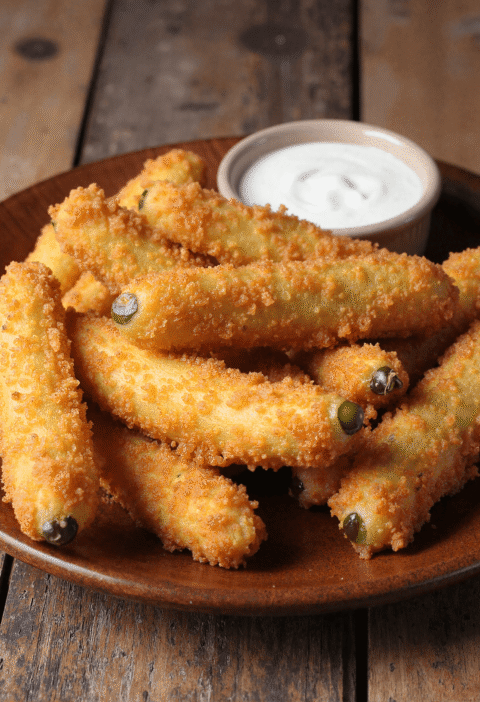 Golden crispy fried pickle spears served on a rustic plate with creamy ranch dip in a ramekin.