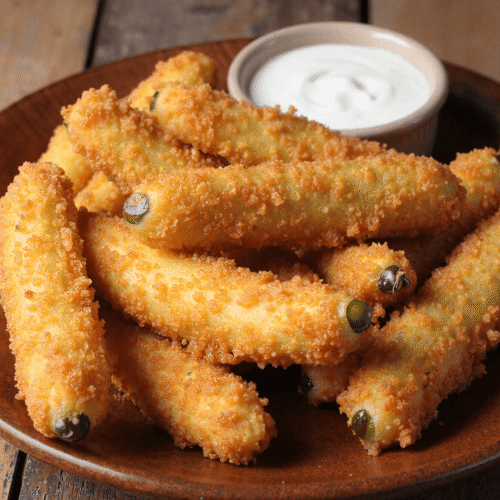 Golden crispy fried pickle spears served on a rustic plate with creamy ranch dip in a ramekin.