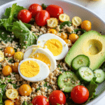 Clean eating egg white power salad with cherry tomatoes, cucumber, quinoa, greens, and avocado in a bowl