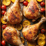 Overhead view of four roasted chicken legs with summer squash and cherry tomatoes on a baking sheet.