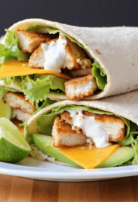 Four chicken avocado ranch wraps arranged on a white plate, each showing grilled chicken, avocado slices, lettuce, cheese, and ranch sauce.