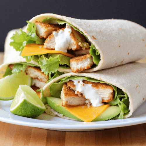 Four chicken avocado ranch wraps arranged on a white plate, each showing grilled chicken, avocado slices, lettuce, cheese, and ranch sauce.