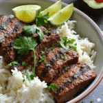 Garlic lime steak sliced over white rice with fresh lime wedges and cilantro garnish
