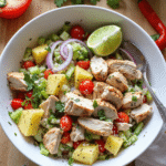 Bowl of tropical Hawaiian chicken salad with grilled chicken, pineapple chunks, cherry tomatoes, cucumber, red onion, and a lime wedge.