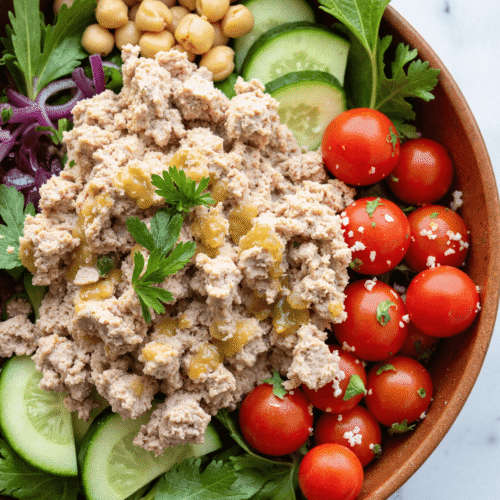 Close-up of a high-protein tuna chickpea salad bowl with cubed tuna, chickpeas, cucumber, and cherry tomatoes.