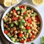 Overhead view of lemon pepper chickpea salad in a white bowl with cucumbers, red bell peppers, and parsley.