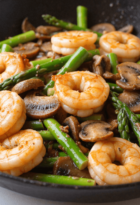 Skillet of shrimp, asparagus, and mushrooms cooked in a light garlic sauce for a high-protein low-carb dinner.