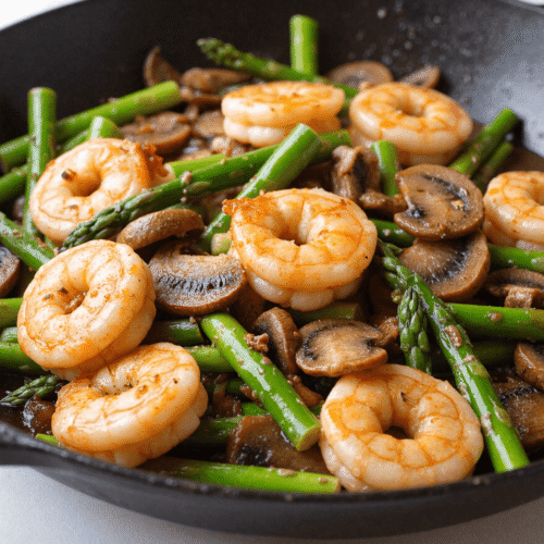 Skillet of shrimp, asparagus, and mushrooms cooked in a light garlic sauce for a high-protein low-carb dinner.