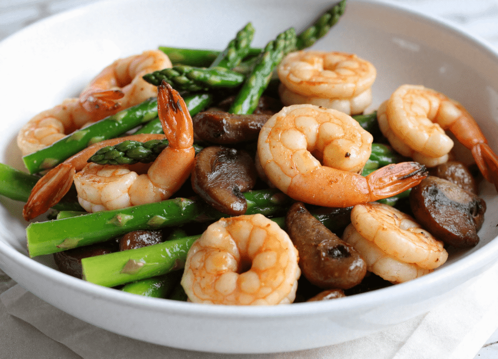 Shrimp, asparagus, and mushrooms served in a white bowl as a healthy, protein-rich stir-fry dinner.