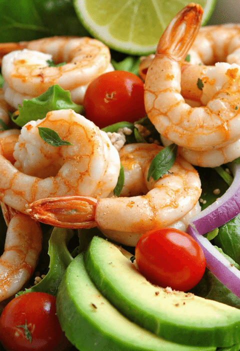 High-protein shrimp and avocado salad with cherry tomatoes, red onion, and mixed greens served with lime.
