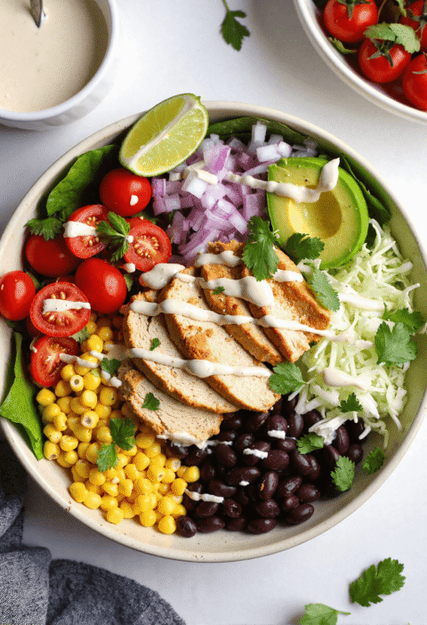 Colorful Southwest Chicken Salad Bowl filled with grilled chicken, black beans, corn, tomatoes, avocado, and Greek yogurt dressing on lettuce.