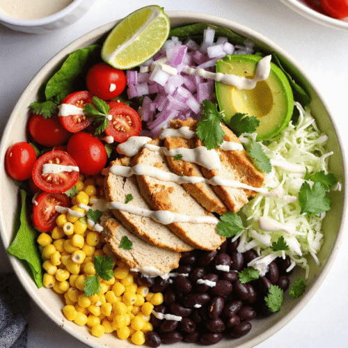 Colorful Southwest Chicken Salad Bowl filled with grilled chicken, black beans, corn, tomatoes, avocado, and Greek yogurt dressing on lettuce.