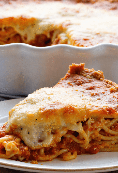 Slice of spaghetti pie on a white plate with layers of pasta, meat sauce, and golden baked cheese topping.