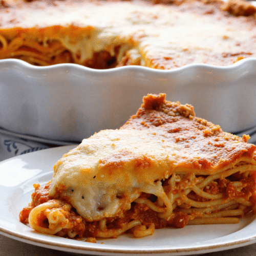 Slice of spaghetti pie on a white plate with layers of pasta, meat sauce, and golden baked cheese topping.