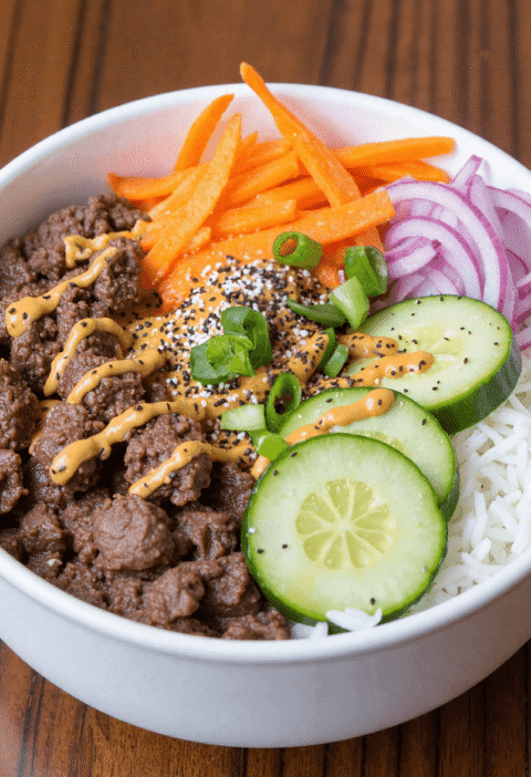 Ground beef dinner bowl with white rice, cucumbers, shredded carrots, red onions, and spicy drizzle – a high-protein, meal prep–friendly comfort food.