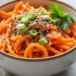 Close-up shot of spiralized carrot salad with sesame seeds, green onion slices, and parsley in a ceramic bowl.