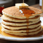 Fluffy vanilla cinnamon buttermilk pancakes stacked high with butter on top and maple syrup dripping down.